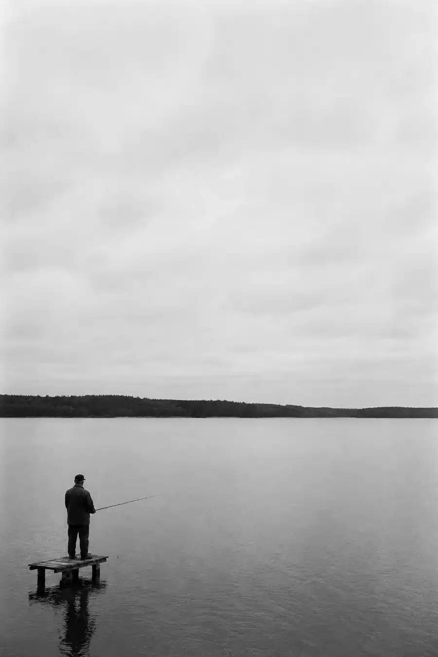 Mies onkimassa laiturilta järvellä, mustavalkoinen kuva