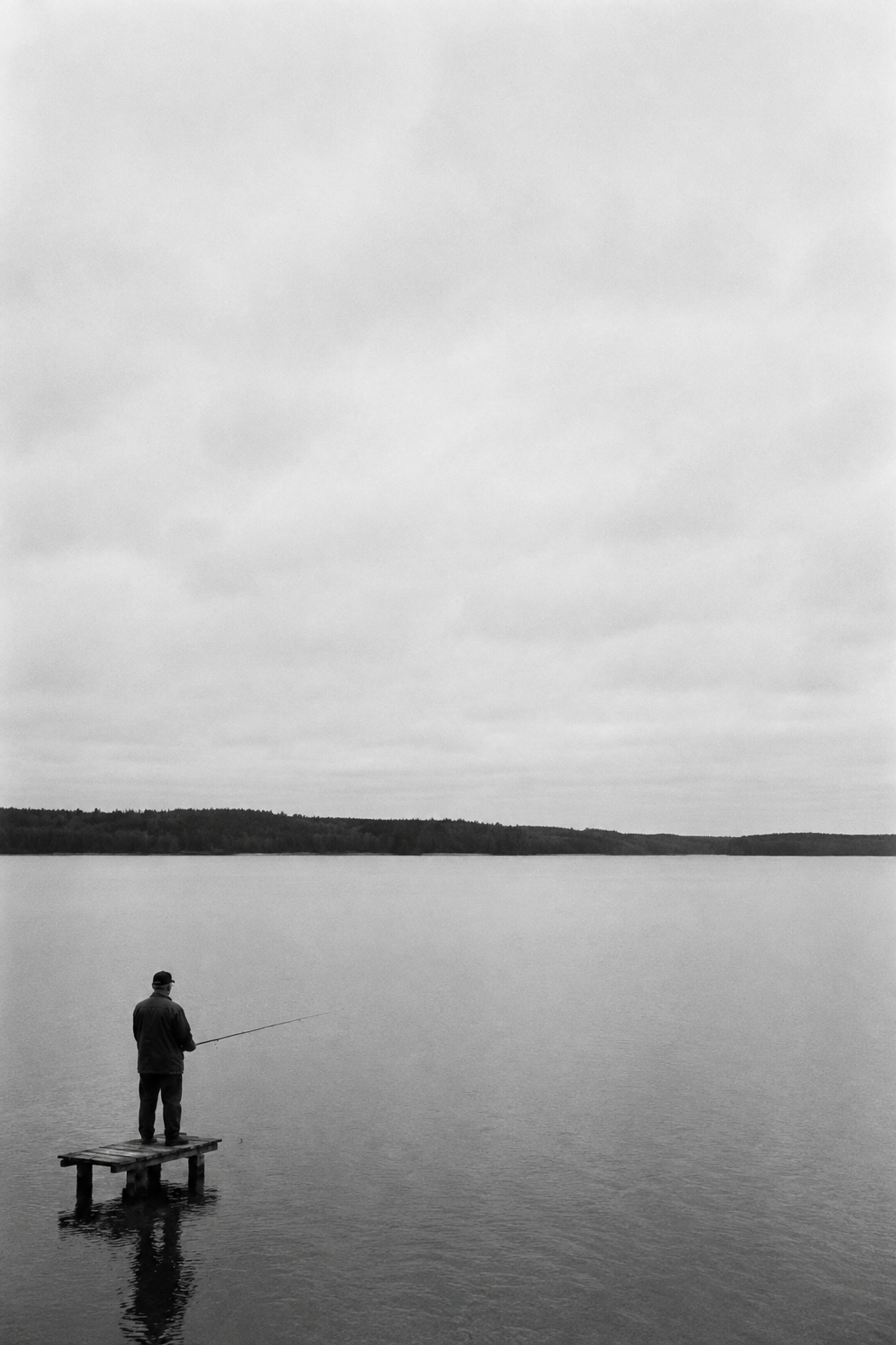 Mies onkimassa laiturilta järvellä, mustavalkoinen kuva